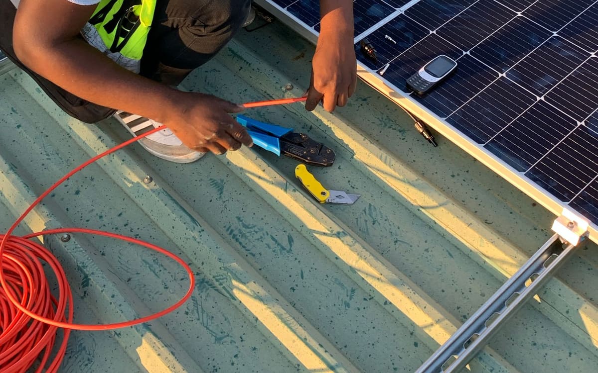 Technician crimping cables beside solar panels on a metal roof